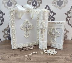 two white wedding guest book with pearls and bows on the front, one has a cross in the middle