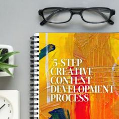 a spiral notebook with the title 5 step creative development process on it next to a clock and plant