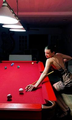 a woman is playing pool in a dark room with red cloths on the table