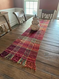 a wooden table topped with a red and yellow plaid runner next to a white vase