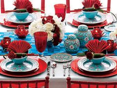 the table is set with red and blue plates, cups, and vases on it