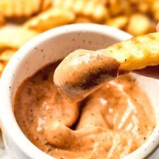 a person dipping something into a small white bowl filled with dip and crackers on the side