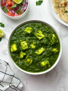 two bowls filled with tofu and spinach on top of a white marble counter