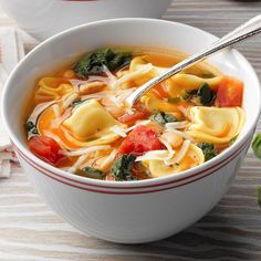 a bowl of pasta soup with spinach and tomatoes on the side, next to a spoon