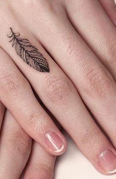 a woman's hand with a small feather tattoo on her left thumb and finger