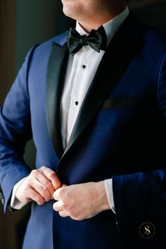 a man in a tuxedo adjusts his bow tie