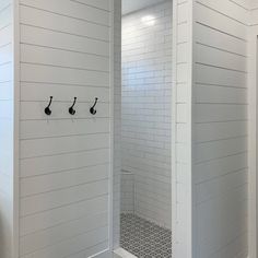 a white bathroom with three black hooks on the wall