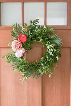 a wreath on the front door with flowers and greenery hanging from it's side