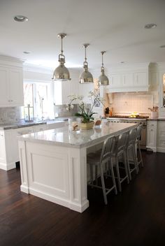 a large kitchen with white cabinets and an island in the middle is surrounded by bar stools