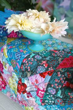 a blue bowl with flowers in it sitting on top of a colorful cloth covered box