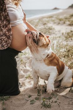 a pregnant woman is petting her dog on the beach while holding it's nose