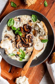 a pan filled with mushrooms and cheese on top of a wooden cutting board next to bread