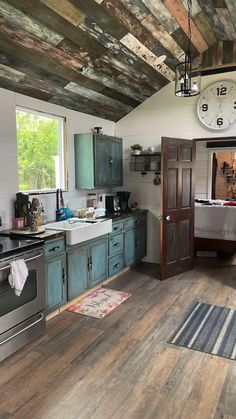 a kitchen with wood flooring and blue cabinetry has a large clock on the wall