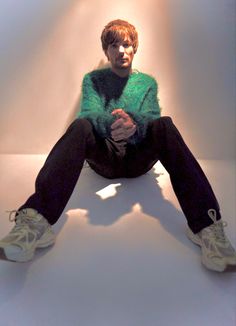 a man sitting on top of a white couch wearing a green sweater and black pants