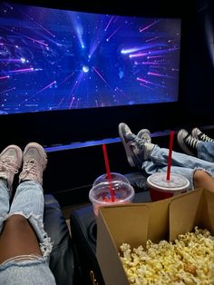 two people sitting in front of a large screen watching movies and eating popcorn at the same time