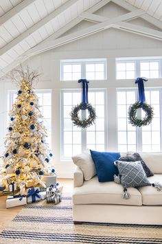 a living room decorated for christmas with a white tree and wreaths on the windows