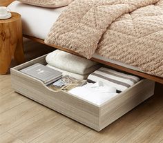 an open drawer underneath a bed in a room with wood floors and white sheets on it