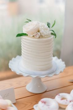 a white cake sitting on top of a table next to cupcakes and flowers