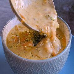 a spoonful of broccoli and cheese soup in a white bowl on a blue plate