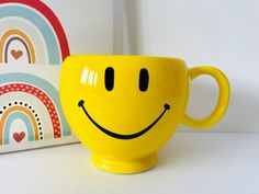 a yellow coffee cup with a smiley face on it next to a rainbow wallpaper