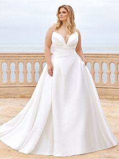 a woman in a white wedding dress standing on a balcony near the ocean with her hands on her hips