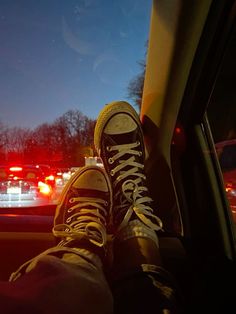 the person is sitting in their car with his feet on the steering wheel and wearing sneakers