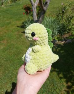 a small crocheted green bird sitting on someone's hand in the grass