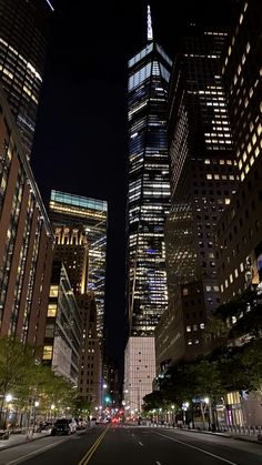 an empty city street at night with skyscrapers lit up in the background and cars driving on the road