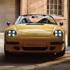 a yellow sports car parked in front of a brick building with its hood up and lights on