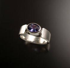 This 5.5 x 7.5 mm Tanzanite oval is bezel-set with tapered cold forged band. The stone is a natural medium dark purple-blue eye clean stone. It weighs about 1ct. Pictured ring is size 7. Specify your ring size in a note to seller at check-out. Modern Oval Tanzanite Sapphire Ring, Modern Oval Tanzanite Ring, Modern Oval Amethyst Ring With Polished Finish, Modern Oval Sapphire Ring With Polished Finish, Modern Oval Sapphire Ring With Tension Setting, Gift Sapphire Ring With Oval Tension Setting, Oval Sapphire Ring With Tension Setting As Gift, Oval Ring, Oval Rings