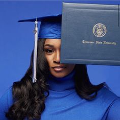 a woman wearing a blue graduation gown and holding up a book to her face with the seal of approval on it