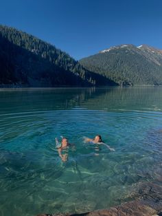 two people swimming in the water near some mountains