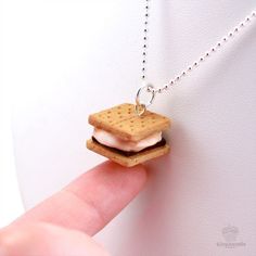 a hand holding a tiny necklace with a small sandwich on it's side,