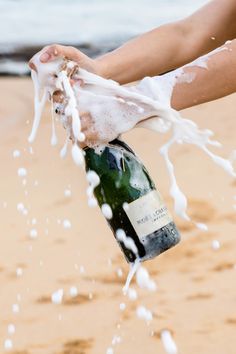 a person is holding a bottle of wine in the sand and splashing it with water