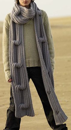 a man standing on top of a sandy beach wearing a scarf and beanie hat