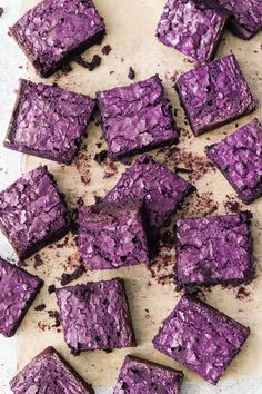 there are many pieces of purple cake that have been cut into squares and placed on a piece of parchment paper