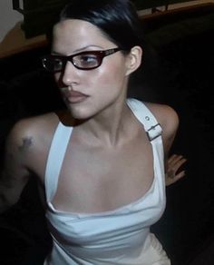 a woman wearing glasses and a tank top is posing for the camera with her arms behind her back