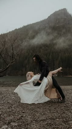 a man and woman are dancing on the ground in front of a mountain with fog