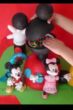 a child's hand reaching for mickey mouse figurines on top of a cake