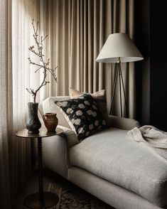 a white couch sitting next to a lamp on top of a wooden table in front of a window