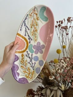 a person holding a plate with flowers and plants in the background on a table top