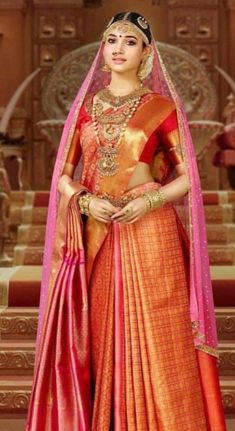 a woman in an orange and pink bridal outfit standing on steps with her hands clasped to her chest