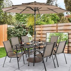 an outdoor dining set with umbrella and table in the middle of a backyard patio area