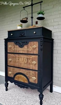 an old dresser is painted black and has gold lettering on the front, along with potted plants