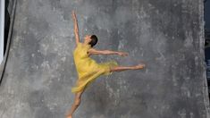 a woman in a yellow dress is doing a ballet move with her arms up and legs spread out