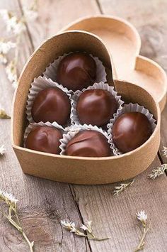 four chocolates in a heart shaped box on a wooden table next to dried flowers