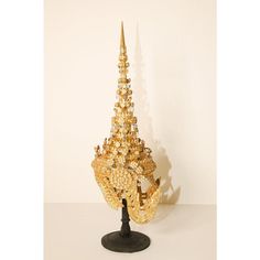 Ceremonial Thai headdress usually worn for wedding or religious ceremonies. Hand-crafted in Thailand. Gilt Thai Ceremonial Headdress circa 20th century. A traditionally modeled design with a conical metal spire at the top, in gilt papier mâché, metal and glass gemstones displayed on a black wooden stand. Dimensions: H 26 in. x W 11 in. x D 9 in. Gold Ceremonial Headpiece With Tall Crown, Traditional Gold Ceremonial Headpieces, Traditional Gold Crown Headpiece, Traditional Gold Headpiece With Tall Crown, Traditional Gold Headpiece With Structured Crown, Traditional Gold Structured Crown Headpiece, Ceremonial Tall Crown Headpiece For Festivals, Religious Ceremony, Head Dress