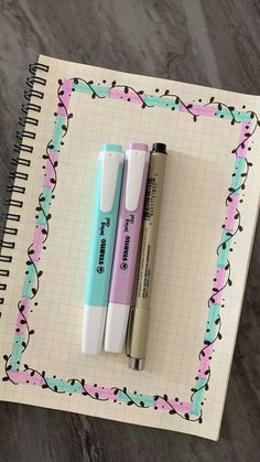 two pens sitting next to each other on top of a notepad with a pen in it