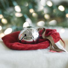 a silver bell sitting on top of a red cloth next to a green christmas tree