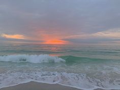 the sun is setting over the ocean with waves coming in to shore and sand on the beach